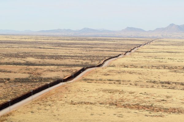 On Public land on the US Mexico border, a long fence stretches across the plains to the mountains in the distance.