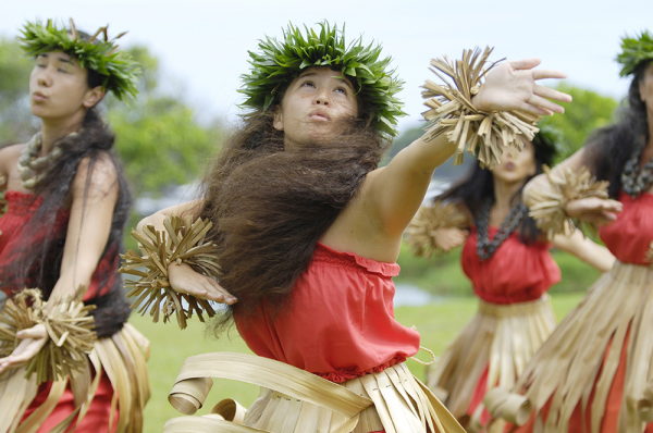 Native Hawaiian hula dancers in red and beige perform a traditional hula dance.
