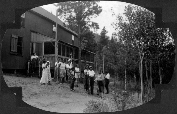 A group of about a dozen young, Black people stand in front of a building surrounded by trees.